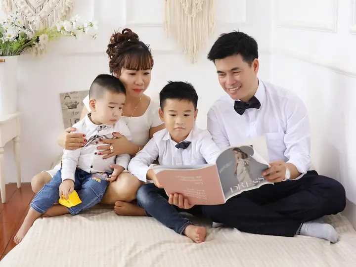 Gia đình bốn người ngồi trên giường, cùng xem một cuốn tạp chí