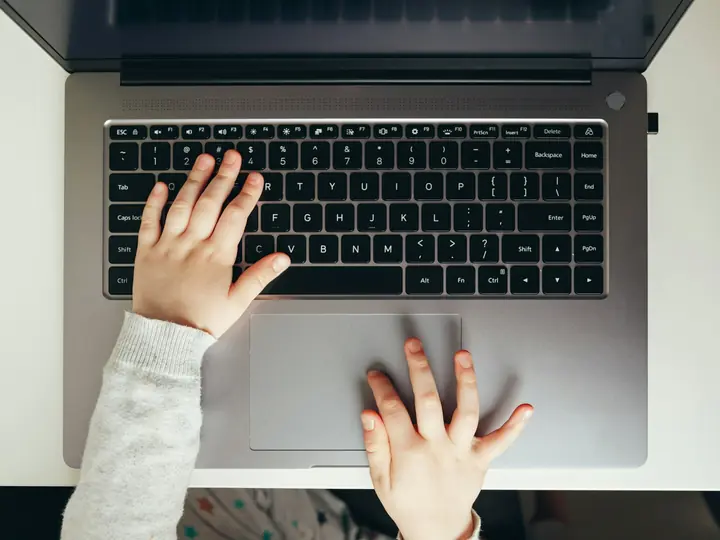Bàn tay trẻ nhỏ gõ trên bàn phím máy tính xách tay